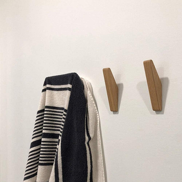 Twee houten wandhaken aan een witte muur naast een zwart-wit gestreepte handdoek die aan een haak hangt. 4
