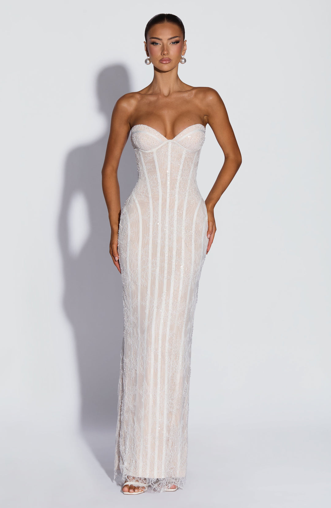 Vooraanzicht van de witte kanten maxi-jurk met kralen en pailletten, model met parelachtige oorbellen en witte sandalen. 9
