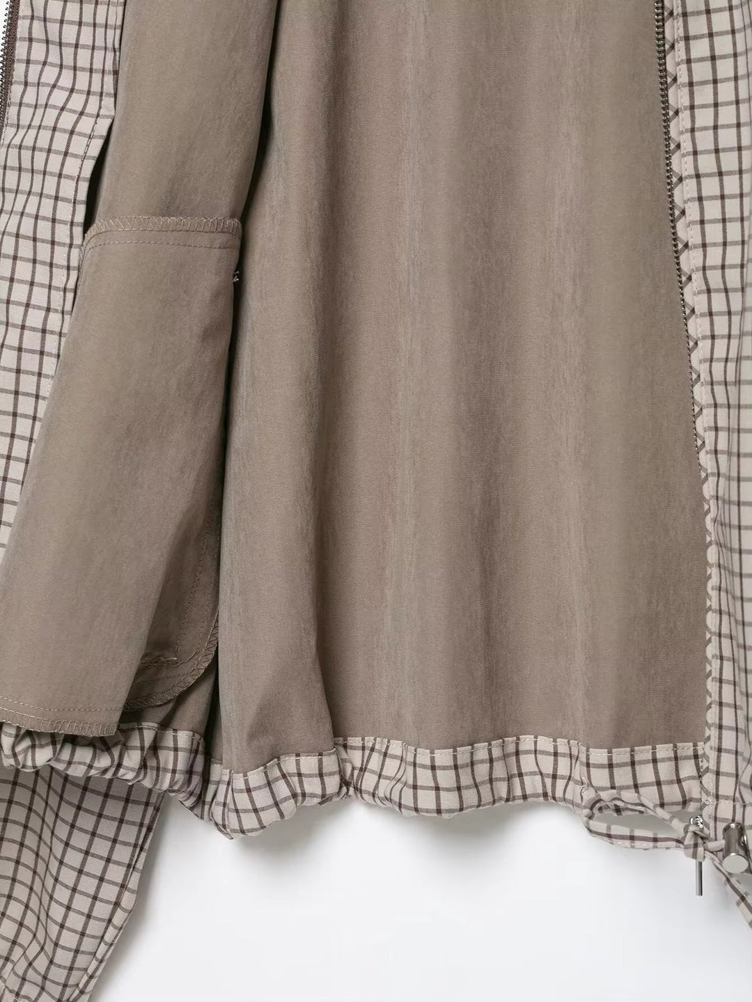 Binnenkant van de jas met effen beige voering, binnenzak en de geruite zoom met trekkoord en metalen koordstopper. 5