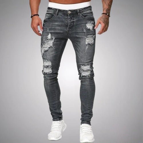 Voorkant van donkergrijze slim fit jeans met gescheurde details op dijen en knieën, gedragen door een model met witte sneakers. 5