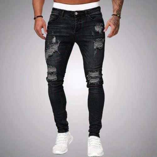 Voorkant van zwarte slim fit jeans met gescheurde delen op dijen en knieën, gedragen door een model met witte sneakers. 1