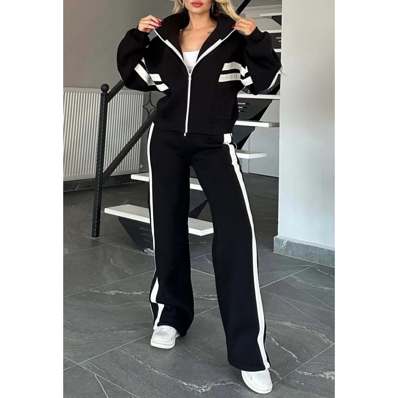 Model in de zwarte set met witte strepen, jack dichtgeritst met opstaande kraag en broek met wijde pijpen. 3