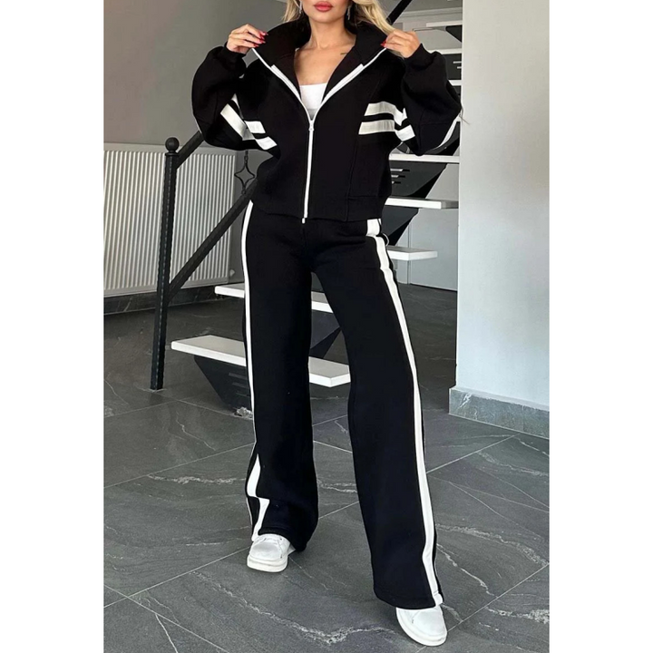 Model in de zwarte set met witte strepen, jack dichtgeritst met opstaande kraag en broek met wijde pijpen. 3