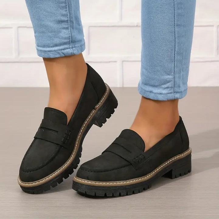 Zwarte loafers met brede profielzool, gedragen met lichtblauwe spijkerbroek, één schoen schuin opgetild. 6