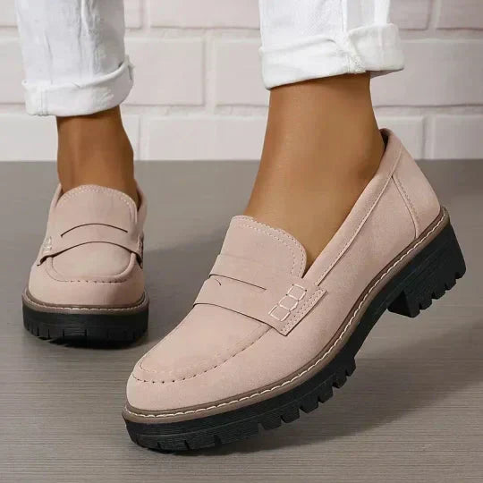 Lichtroze loafers met stiksels en zwarte plateauzool, gedragen met witte broek, close-up vanaf de zijkant. 8