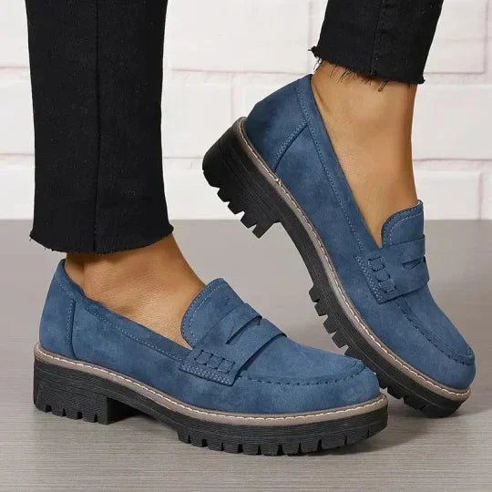 Blauwe loafers met zwarte plateauzool, gedragen met zwarte broek, beide schoenen schuin van boven gezien. 9