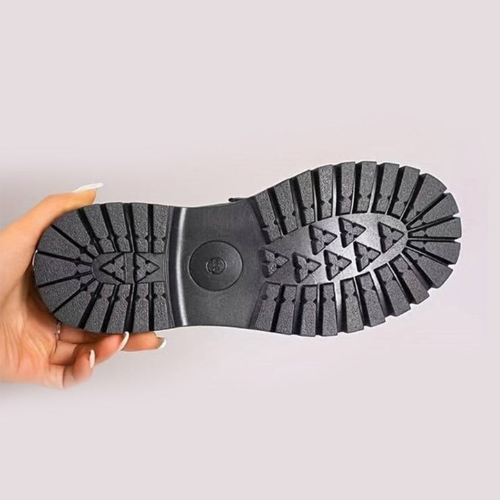 Onderkant van de loafer in de hand gehouden, met de zwarte zool met diep profiel en een rond logo in het midden. 10