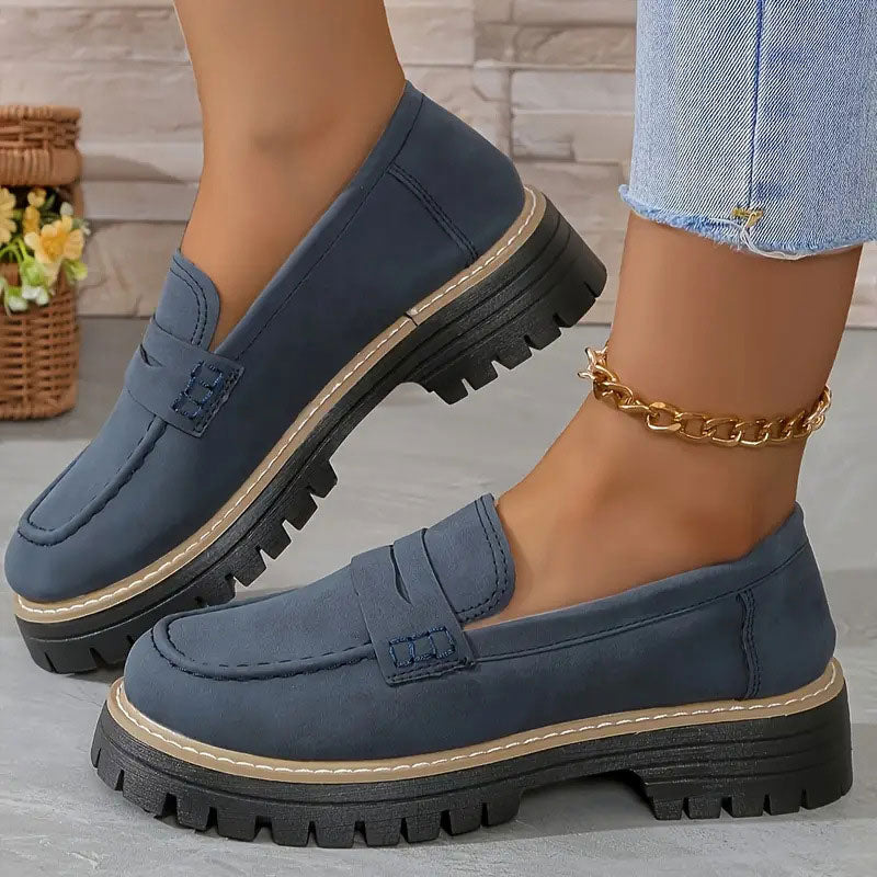 Donkerblauwe loafers met beige zoolrand en zwarte plateauzool, gedragen met gouden enkelbandje. 16