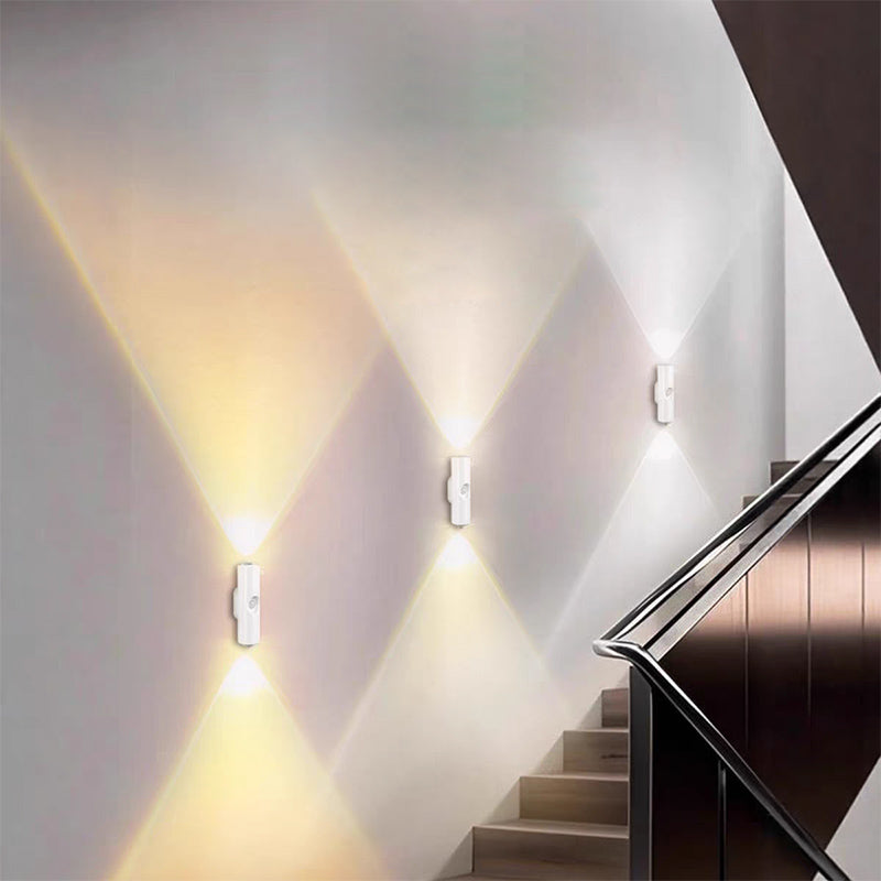 Drie witte wandlampen langs een trap, met warm wit licht dat in driehoeken omhoog en omlaag op de muur valt 8