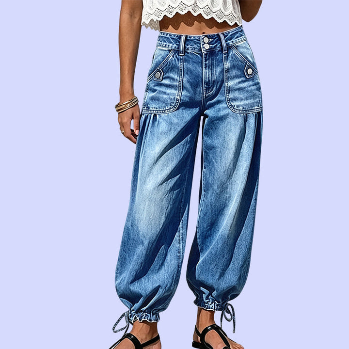 Close-up van het onderlichaam in de blauwe barreljeans met hoge taille, dubbele knoopsluiting, opgestikte zakken en gestrikte zoom op lila achtergrond. 10