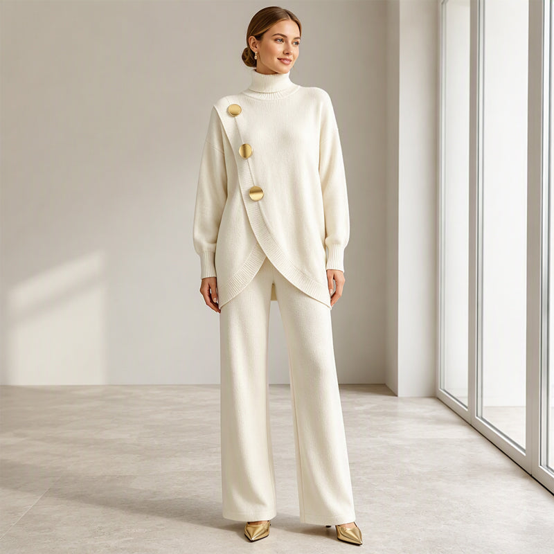 Model in crèmewitte gebreide set, volledig in beeld met gouden knopen, wijde broek en gouden puntschoenen, zonder handtas. 7