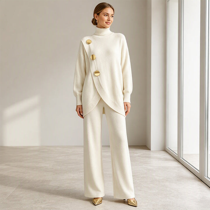 Model in crèmewitte gebreide set, volledig in beeld met gouden knopen, wijde broek en gouden puntschoenen, zonder handtas. 7