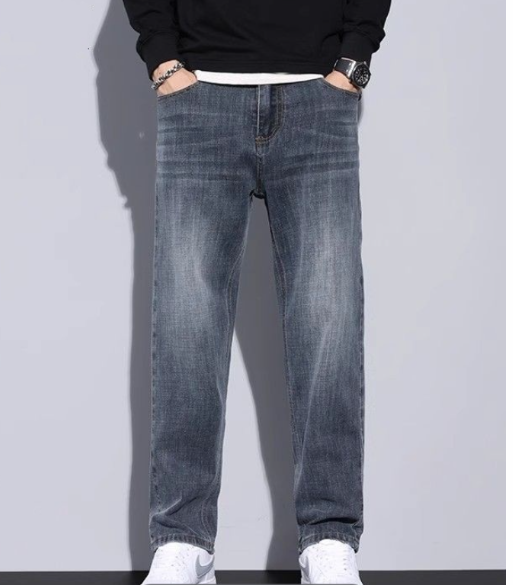 Grijsblauwe jeans gedragen met zwarte trui, beide handen in de zakken, model getoond tot de witte sneakers. 11