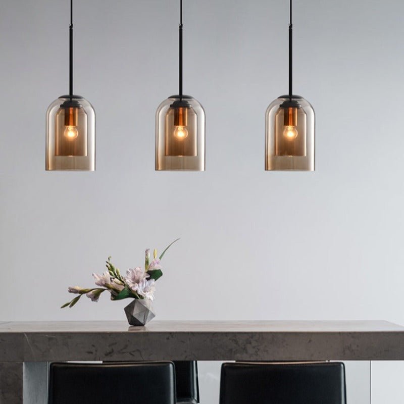 Drie amberkleurige hanglampen boven een stenen eettafel met zwarte stoelen en een bosje bloemen 6