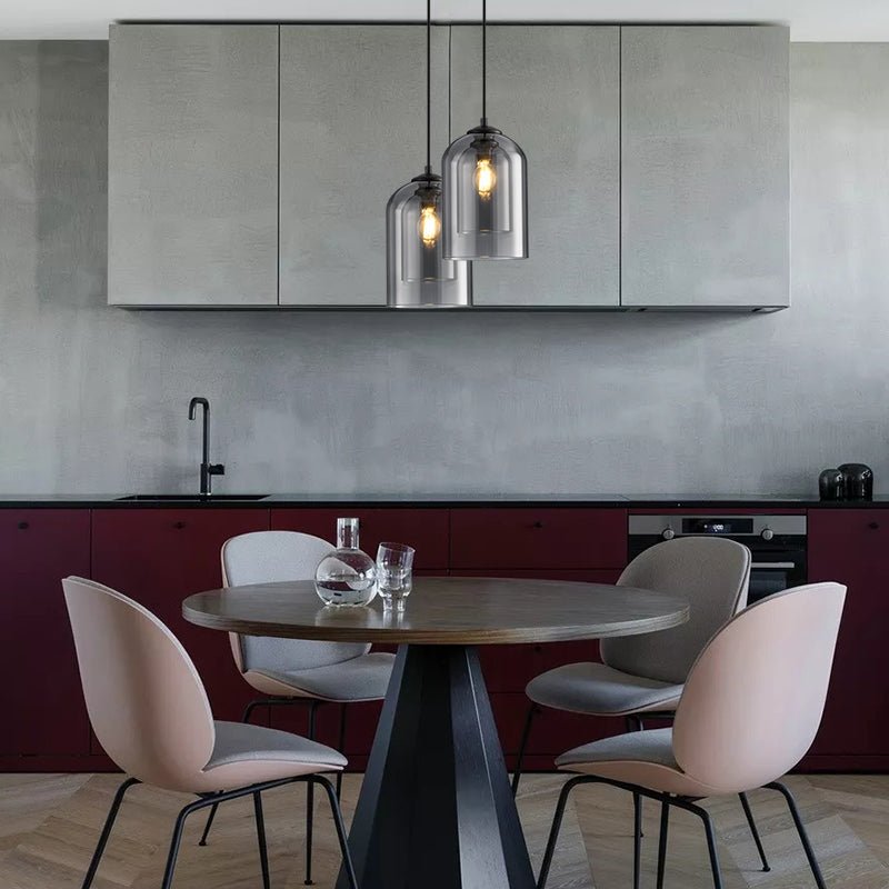 Twee rookgrijze hanglampen op verschillende hoogte boven een ronde eettafel met roze stoelen in een keuken 7