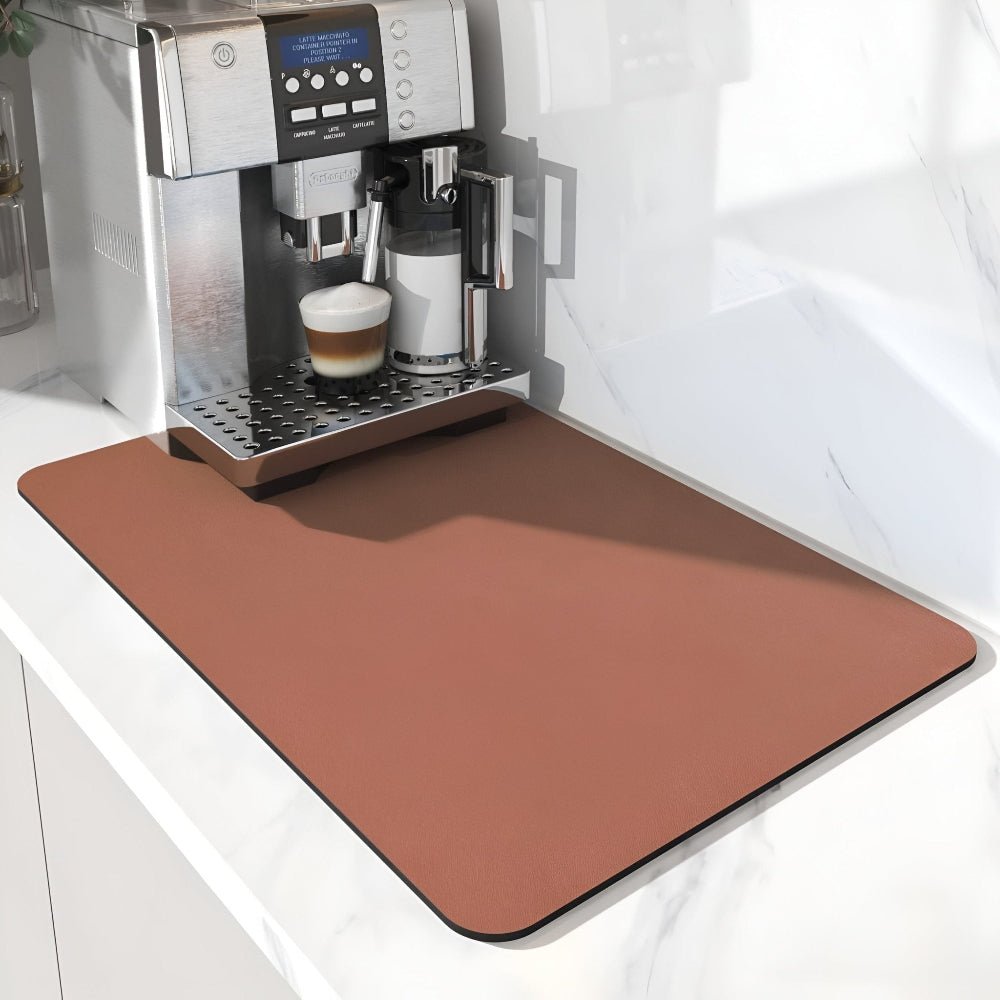 Terracottakleurige mat onder een koffiemachine met melkkan en cappuccino, op een wit marmeren aanrechtblad. 10
