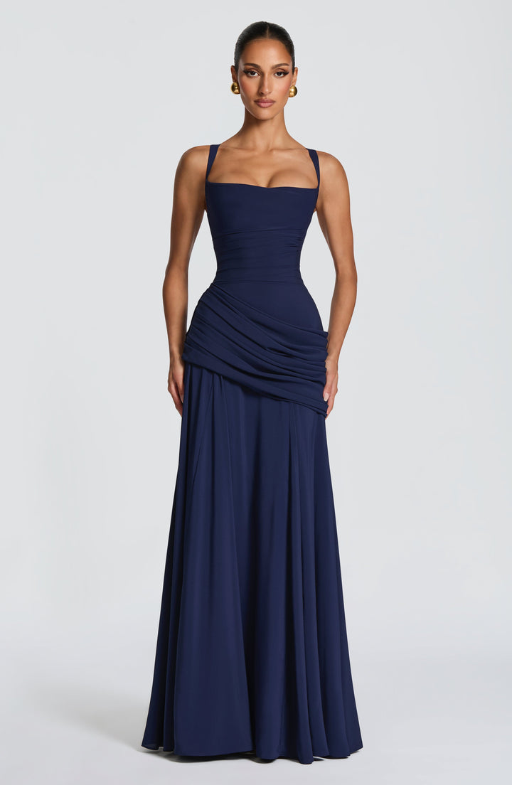 Marineblauwe maxi-jurk met vierkante halslijn en gedrapeerde heupen, van voren gedragen door een model met gouden oorbellen. 7
