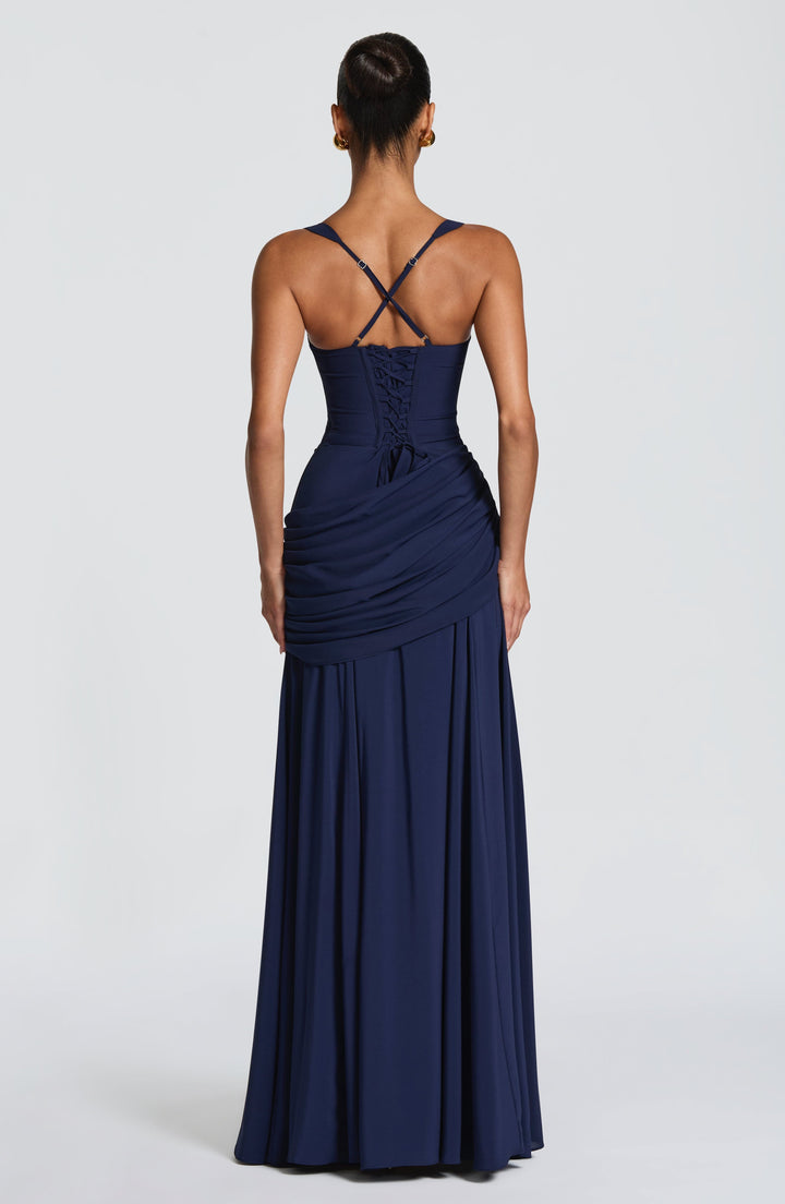 Achterkant van de marineblauwe maxi-jurk met veterrug, gekruiste verstelbare bandjes en gedrapeerde zijkant, gedragen door een model. 11