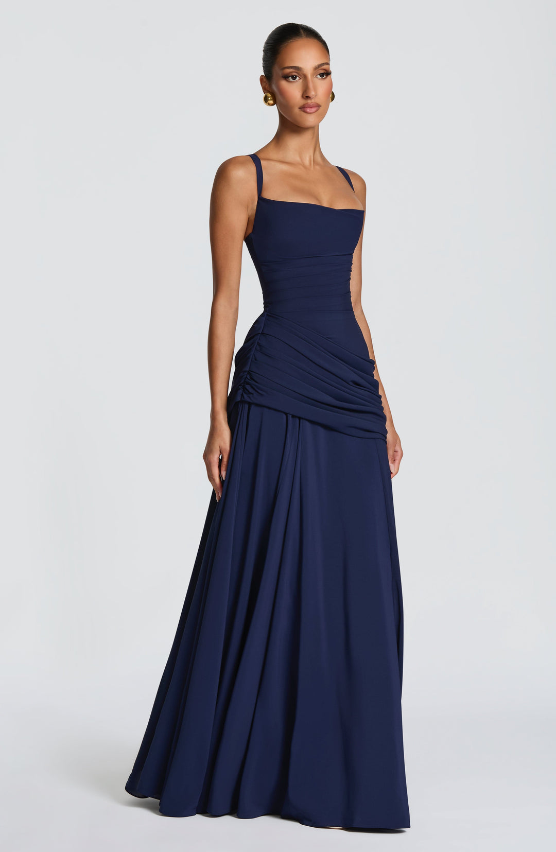Marineblauwe maxi-jurk van opzij gefotografeerd op een model, met dunne bandjes, geplooide taille en wijd uitlopende rok. 12