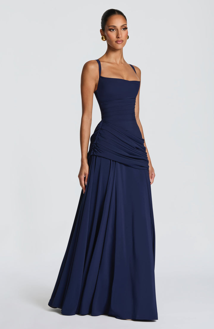 Marineblauwe maxi-jurk van opzij gefotografeerd op een model, met dunne bandjes, geplooide taille en wijd uitlopende rok. 12
