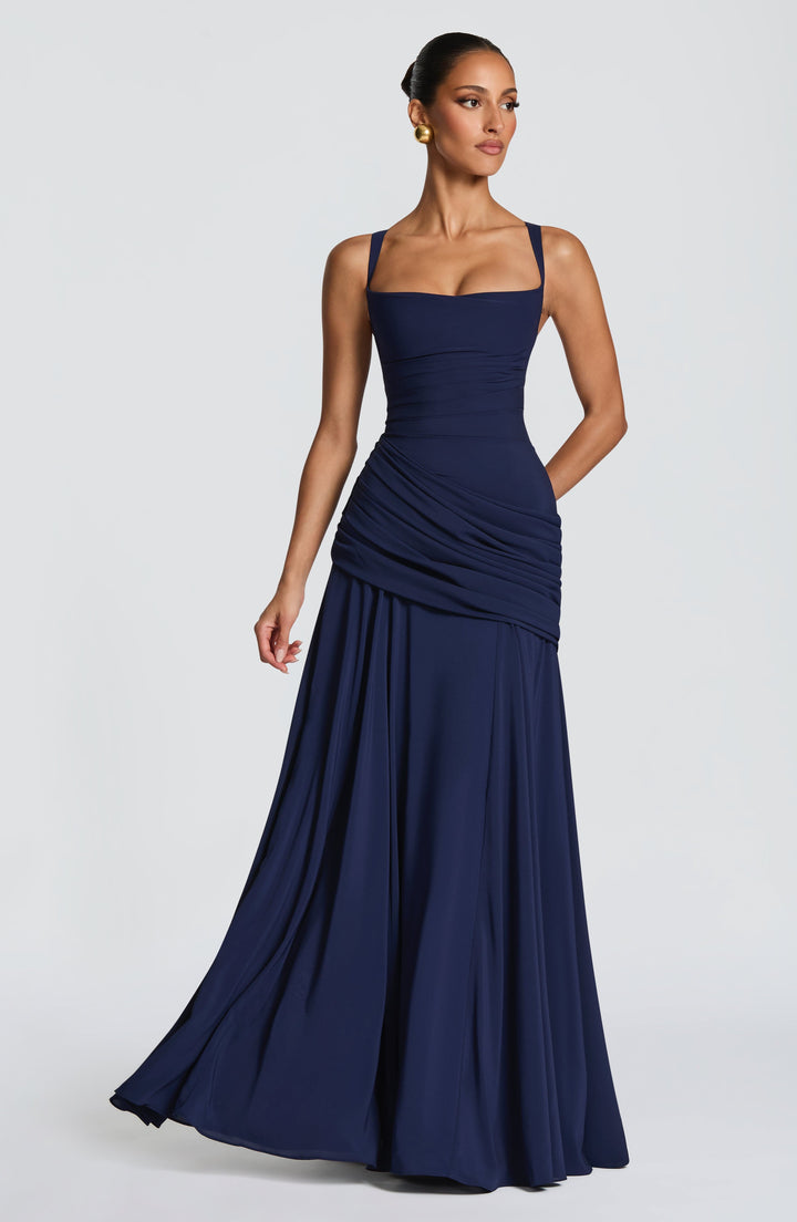 Marineblauwe maxi-jurk in driekwartaanzicht op een model met opgestoken haar, met de rok licht in beweging. 8