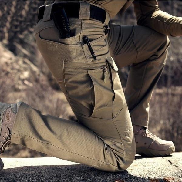 Close-up van een knielende man in beige broek, met zijzak met rits en opgeborgen pen 2