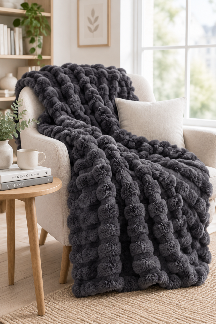 Donkergrijze pluizige bolletjesdeken over een lichte fauteuil, naast een houten bijzettafel met mok 14