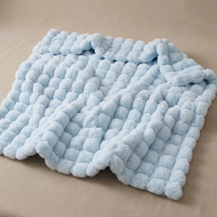 Lichtblauwe pluche deken met bobbelstructuur, uitgespreid op een beige ondergrond 17