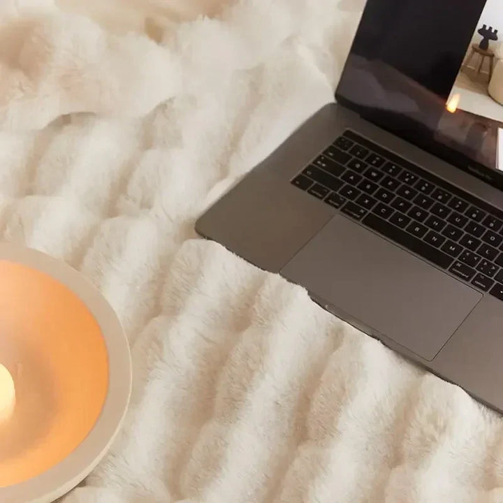 Close-up van een witte pluche deken met een laptop en een kaars in een schaaltje 8