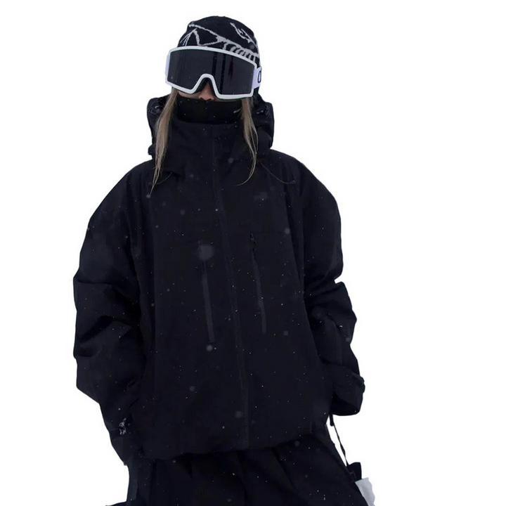 Model in zwarte sneeuwjack met capuchon en hoge kraag, frontaal gefotografeerd met skibril, in sneeuwval. 3