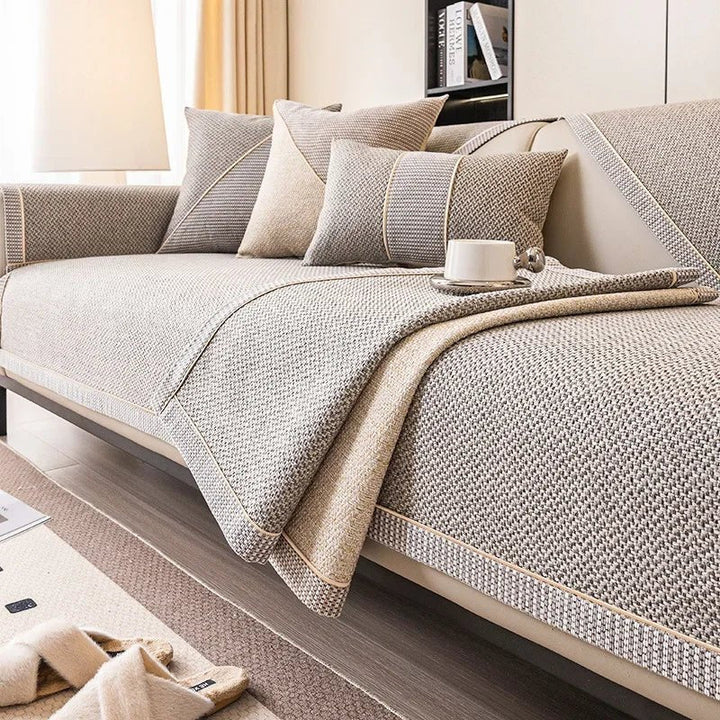 Taupe bankhoes met een omgeslagen stuk op de zitting, waardoor de beige onderzijde zichtbaar is naast kussens en een kopje. 5