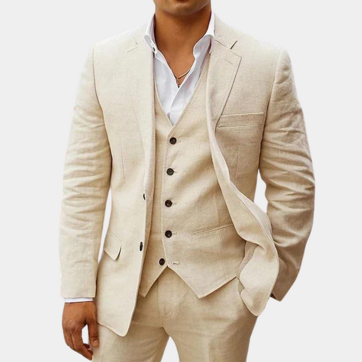 Model draagt het pak in beige met wit overhemd, een hand in de zak, gilet met vijf knopen zichtbaar. 1