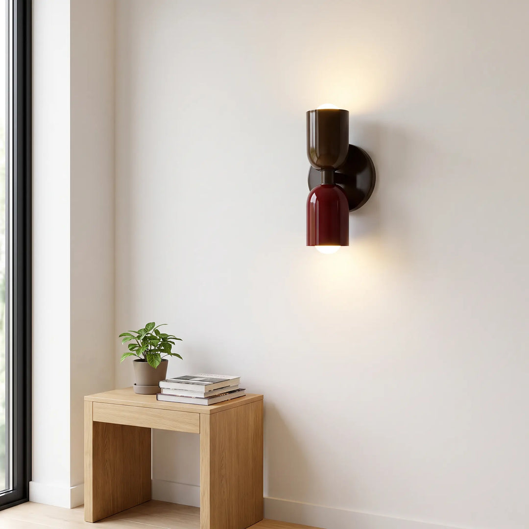 Wandlamp in donkerbruin en bordeauxrood naast een groot raam, boven een houten krukje met boeken en een kamerplant. 10