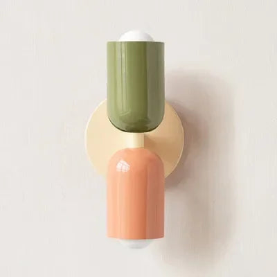 Close-up van een wandlamp met een olijfgroene bovenkap, perzikkleurige onderkap en crème wandplaat tegen een lichte muur. 19