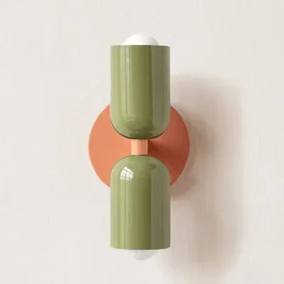 Wandlamp met twee glanzende groene kappen op een ronde oranje montageplaat, tegen een lichte muur. 21