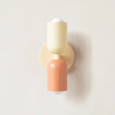Close-up van een wandlamp in crème en perzik tegen een lichte muur, met twee bolvormige lampen. 16