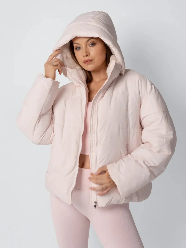 Model in roze pufferjack met capuchon over het hoofd en hand aan de rand van de capuchon 6