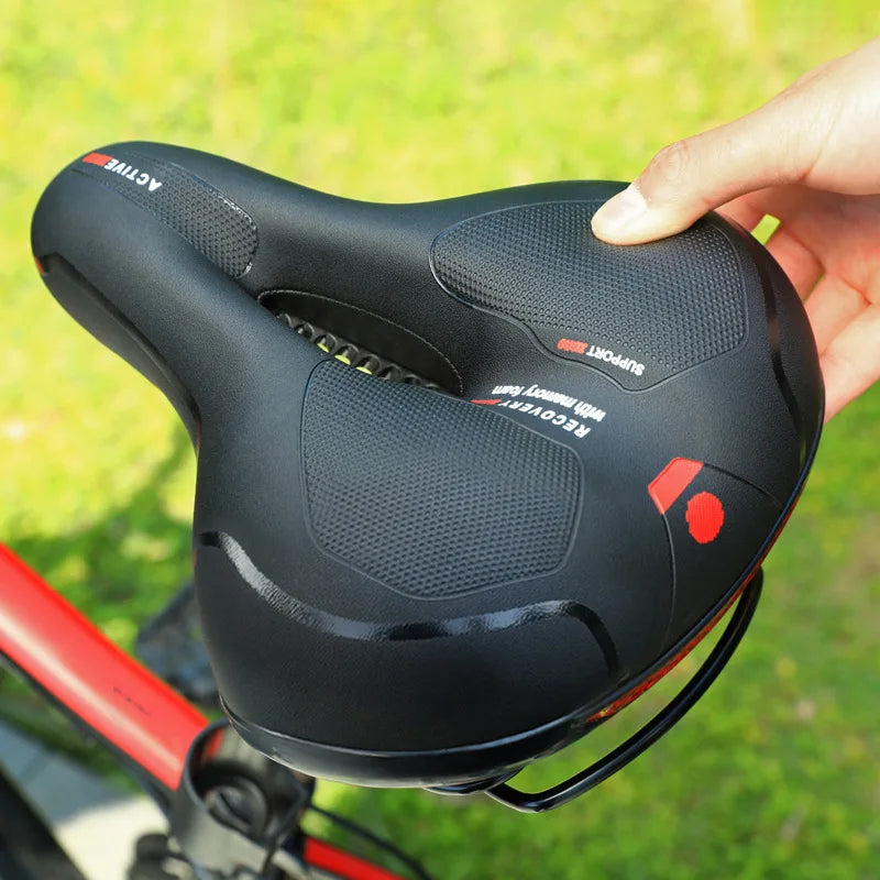 Hand drukt op het zwarte zadel met uitsparing en antislip vlakken, gehouden boven een grasveld naast een fietsframe. 5