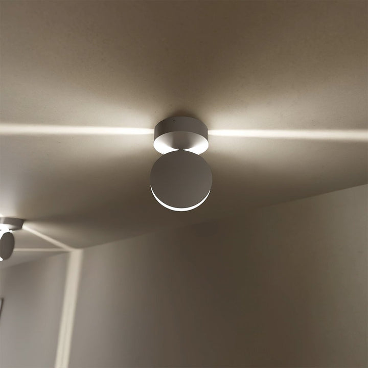 Witte plafondlamp met ronde draaibare kop van dichtbij, die twee horizontale lichtstralen over het plafond werpt. 3